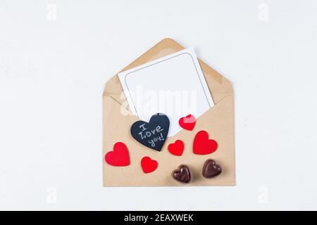 Maquette de Saint-Valentin. Carte d'amour. Carte en papier avec enveloppe et bonbons au chocolat sur fond de table blanc. Plan de travail, vue de dessus, place pour l'espace Banque D'Images