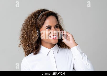 Service souriant femme afro-américaine sourit de porter des écouteurs le studio du personnel du centre d'appels a été tourné sur fond gris clair Banque D'Images