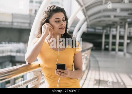 Jeune femme hispanique portant un casque à l'écoute de la musique avec les yeux fermé dans un passage couvert de la ville Banque D'Images