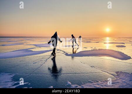 Les gens patinent en silhouette au lac gelé contre magnifique lever de soleil orange Banque D'Images