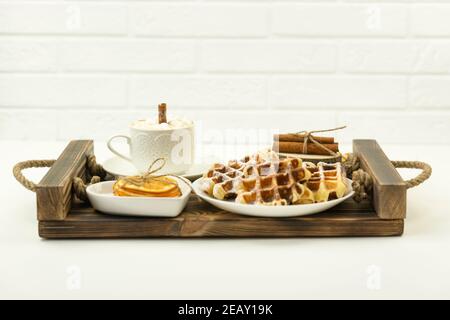 Petit-déjeuner servi tôt avec des guimauves et un bâton de cannelle Et des gaufres belges reposent sur un plateau en bois Banque D'Images