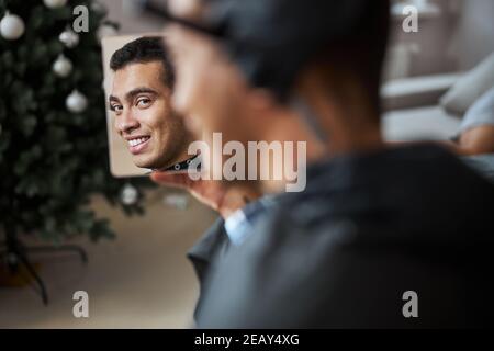 Heureux homme souriant avec un beau sourire en admirant ses nouveaux cheveux style dans le salon de beauté Banque D'Images