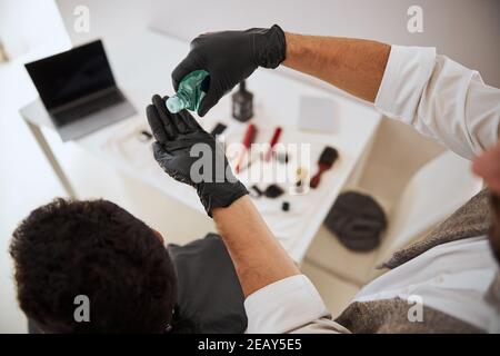 Homme mains dans des gants tenant l'assainisseur au-dessus du bureau avec différents outils pour cheveux Banque D'Images