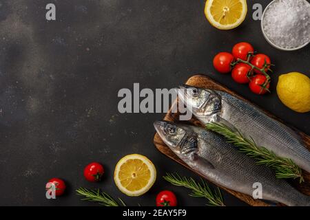 Deux poissons de mer frais avec romarin et légumes sur table noire. Concept de fruits de mer. Banque D'Images