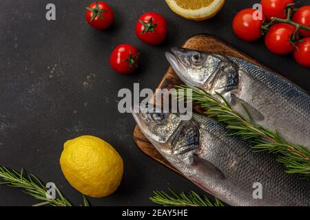 Deux poissons de mer frais avec romarin et légumes sur table noire. Concept de fruits de mer. Banque D'Images