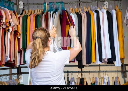 la femme choisit des vêtements qui passent par le diffuseur dans le magasin du marché. vue arrière Banque D'Images