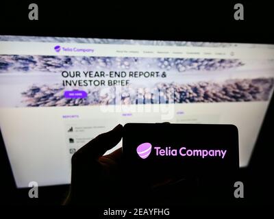 Personne tenant un smartphone avec le logo du fournisseur suédois de télécommunications Telia Company AB sur l'écran devant le site Web. Mise au point sur l'affichage du téléphone. Banque D'Images