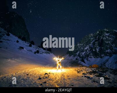 Homme avec une guirlande orange lumineuse dans les montagnes d'hiver à ciel sombre Banque D'Images