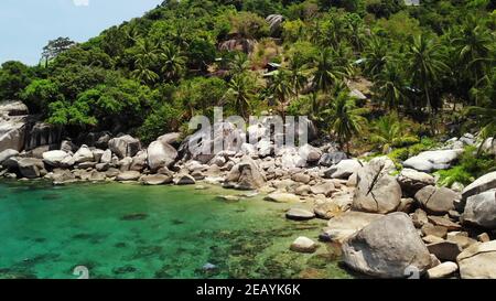 Palmiers tropicaux et pierres sur une petite plage. Beaucoup de palmiers exotiques verts poussant sur la côte rocheuse près de la mer bleue calme dans la baie de Hin Wong le jour ensoleillé en Thaïlande. Banque D'Images