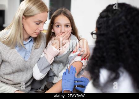 Pédiatre et patient à domicile. Gros plan de la jolie fille de l'adolescence, peur et peur de l'injection, étant soutenu par sa mère, tandis que la femme médecin fait Banque D'Images