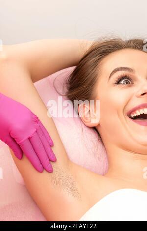 Jeune femme pendant l'examen de l'aisselle avant la procédure de cirage riant dedans un salon de beauté Banque D'Images