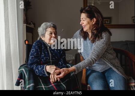 Une vieille femme malade en fauteuil roulant à côté d'une fille souriante. Troisième âge, concept de soins à domicile. Banque D'Images