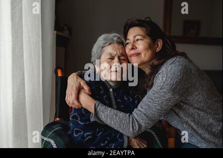 Portrait d'une femme en fauteuil roulant embrassant sa fille avec un visage positif. Troisième âge, concept de soins à domicile. Banque D'Images