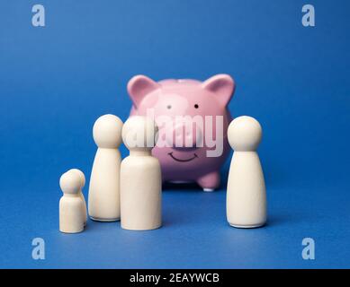 figurines de famille en bois sur fond de piggy en céramique rose sur fond bleu, concept de sauvegarde Banque D'Images