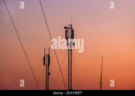 Tour avec un transmetteur de signal mobile sur le fond d'un ciel orange sans nuages le matin. Banque D'Images
