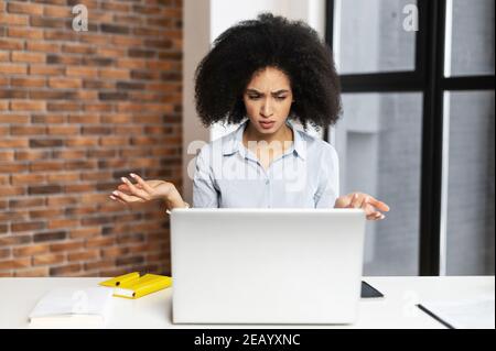 Une jeune femme d'affaires afro-américaine confuse et surprise a reçu des nouvelles inattendues, assise à la réception du bureau, levant la main et regardant Banque D'Images