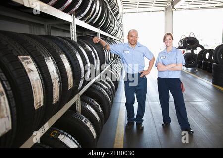 Portrait d'un homme souriant et d'une femme mécanicien par un rack de pneus dans un atelier Banque D'Images