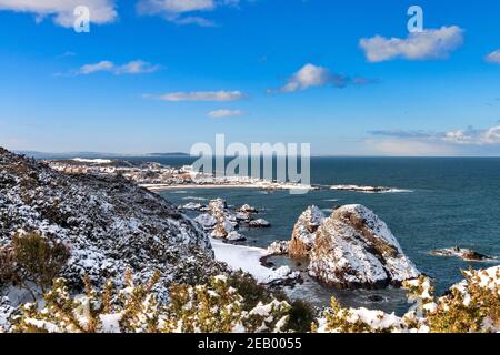 FINDOCHTY MORAY FIRTH SCOTLAND VUE D'HIVER SUR LA NEIGE DE LA BAIE FALAISES COUVERTES ROCHERS MAISONS DE VILLAGE ET KIRK SUR LA COLLINE Banque D'Images