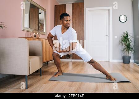 Vue de face d'un homme afro-américain souriant qui fait une fente latérale exercice à la maison Banque D'Images