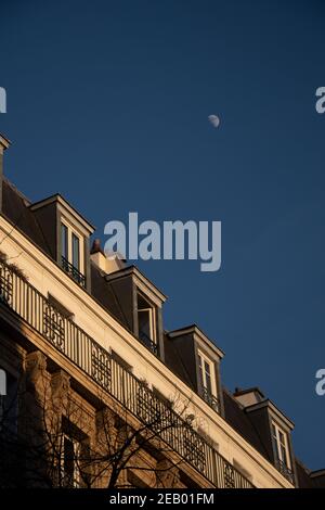 Maison sous la lune. Maison parisienne typique avec mansardes au coucher du soleil doré et lune blanche dans le ciel bleu foncé en hiver. Paris, France. Ville romantique Banque D'Images