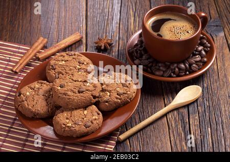 Tasse de café et biscuits au chocolat avec noix dans l'assiette pour le petit déjeuner sur une table en bois sombre Banque D'Images