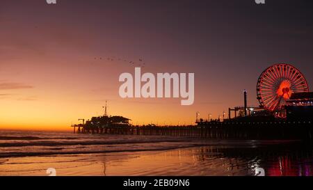 Des vagues de crépuscule contre une grande roue lumineuse classique, parc d'attractions sur la jetée de Santa Monica pacific Ocean Beach Resort. Symbole emblématique de l'été o Banque D'Images