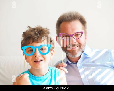 Adorable garçon drôle et papa ont des verres en papier sur des bâtons. La famille se prépare à célébrer le jour des Fools d'avril. Banque D'Images