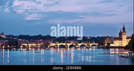 Le coucher du soleil se trouve au bord de la rivière de Prague. Image panoramique du pont Charles illuminé et des bâtiments au bord de la rivière avec tour d'horloge Banque D'Images