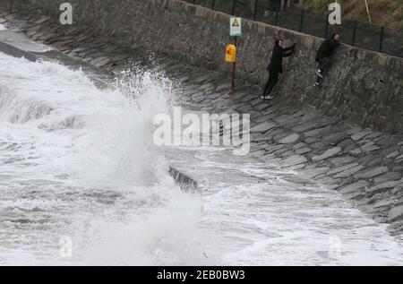 Deux hommes escaladent un mur pour éviter de briser les vagues le long du front de mer à Seapoint Beach à Dublin comme met Eireann ont émis deux avertissements météorologiques, y compris des vents forts à gales du sud-est en conjonction avec la pluie, la grésil et la neige. Date de la photo : jeudi 11 février 2021. Banque D'Images
