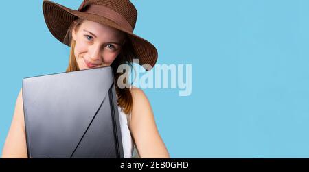 Bannière,format long. Jolie fille avec chapeau posant avec ordinateur portable regardant la caméra sur un fond bleu avec espace publicitaire latéral. Banque D'Images