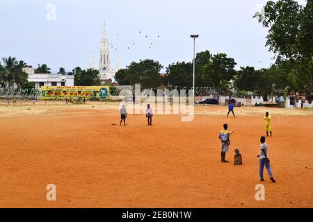 Kanyakumari, Tamil Nadu, Inde - janvier 2017 : des garçons indiens jouent au cricket sur le terrain de jeu du parc. Église catholique blanche en arrière-plan. Banque D'Images