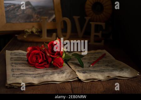Roses rouges de la Saint-Valentin sur des feuilles de musique vintage avec le mot amour. Banque D'Images