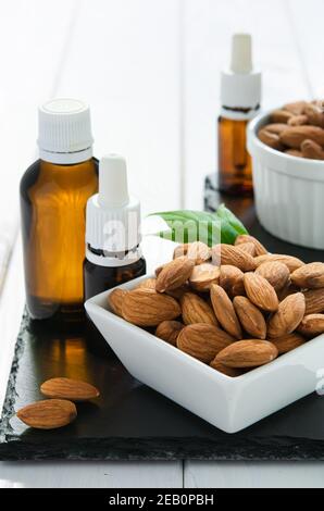 amandes en plaque blanche et bouteilles de verre avec huile sur un plateau noir sur une table en bois Banque D'Images