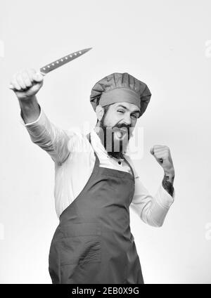 Cuisinez avec succès le visage dans un tablier bordeaux et un chapeau de chef. Cuisine et concept culinaire professionnel. Chef tient le couteau bleu vif vers le haut. Homme avec une barbe en uniforme de cuisinier isolé sur fond blanc. Banque D'Images