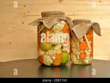 Concept de deux pots de cornichons de saison avec tomates vertes crues de couleur, carotte d'orange et chou-fleur blanc sur fond de bois naturel. Vue avant Banque D'Images