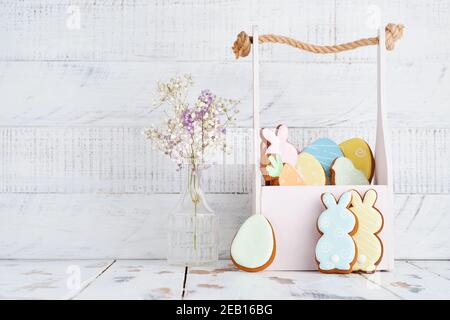 Carte de vœux de Pâques avec lapins colorés, œufs, poulets et carottes, panier de biscuits au pain d'épice devant un mur en bois. Maquette. Vue de dessus. Banque D'Images