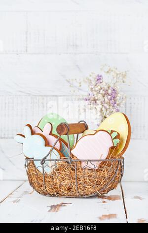 Carte de vœux de Pâques avec lapins colorés, œufs, poulets et carottes, panier de biscuits au pain d'épice devant un mur en bois. Maquette. Vue de dessus. Banque D'Images