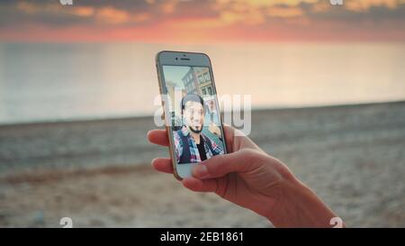Gros plan sur la réalisation d'appels vidéo avec un smartphone sur le bord de mer. Le jeune homme est en discussion. Banque D'Images
