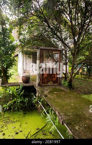 La maison de deux étages est située à l'arrière de la route et du canal rempli d'algues Banque D'Images