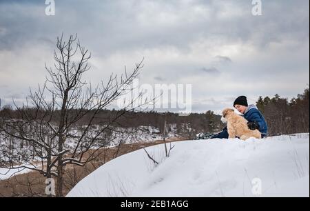 Un adolescent et son chien assis au sommet d'une colline enneigée le jour d'hiver. Banque D'Images