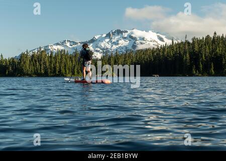 Pédalo-randonnée femelle anonyme sur le lac près de la pente de montagne et forêt verte Banque D'Images