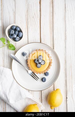 Croûte de noix Tartlet avec garniture de caillé de citron, recouvert de bleuets frais et arrosé de sucre en poudre sur fond de bois rustique Banque D'Images