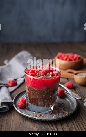 Dessert végétalien santé super-alimentaire, gâteau de graines de chia au cacao foncé avec purée de framboise, recouvert de baies fraîches et de copeaux de chocolat dans un pot en verre Banque D'Images