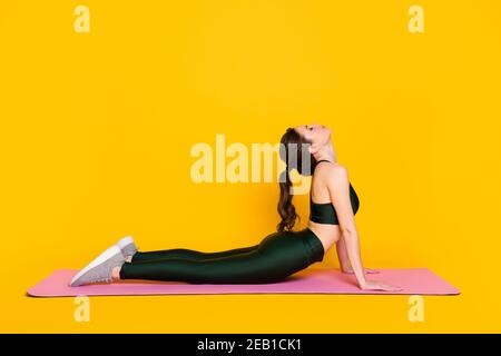 Profil côté plein corps vue de la jolie petite fille bendy mince instructeur effectuant la mise en forme de tous les jours flexion isolée sur couleur jaune vif arrière-plan Banque D'Images