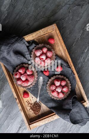 Tartelettes en croûte de cacao remplies de mousse au chocolat noir à base de crème fouettée et de purée de framboises, recouvertes de baies fraîches, arrosées de poudre Banque D'Images