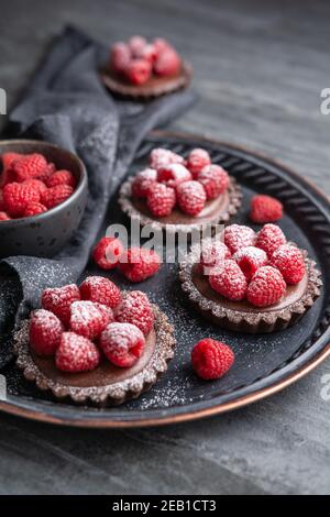 Tartelettes en croûte de cacao remplies de mousse au chocolat noir à base de crème fouettée et de purée de framboises, recouvertes de baies fraîches, arrosées de poudre Banque D'Images