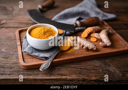 Ingrédient alimentaire anti-inflammatoire, poudre de curcuma dans un bol en céramique et racine fraîche sur fond rustique en bois Banque D'Images