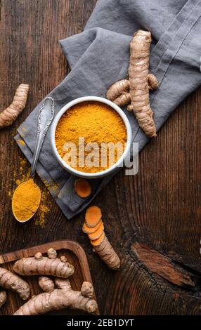 Ingrédient alimentaire anti-inflammatoire, poudre de curcuma dans un bol en céramique et racine fraîche sur fond rustique en bois Banque D'Images