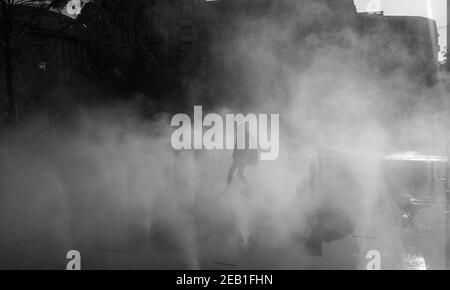 Silhouette floue d'une jeune fille méconnue jouant dans la brume d'eau de fontaine le jour de l'automne. Place des Halles, Paris, France. Photo en noir et blanc. Banque D'Images