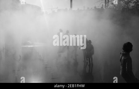 Enfants méconnaissables (vue arrière, silhouettes) jouant dans la brume d'eau de fontaine le jour de l'automne. Place des Halles, Paris, scène urbaine. France. Noir et blanc Banque D'Images